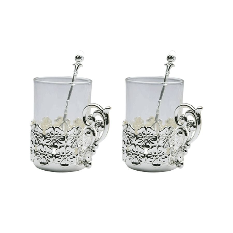 a set of two silver mugs with flower motif and designer handles accompanied by sleek spoons