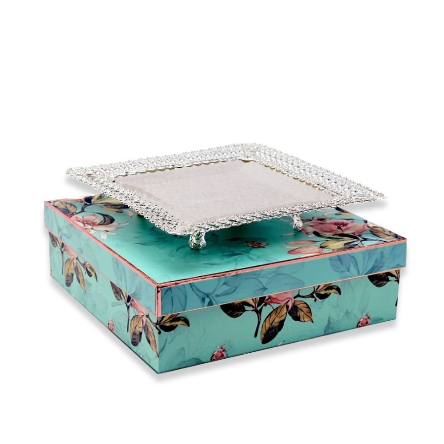 a simplistic yet enchanting square silver tray with intricate border and designer legs kept on top of a beautiful gift box